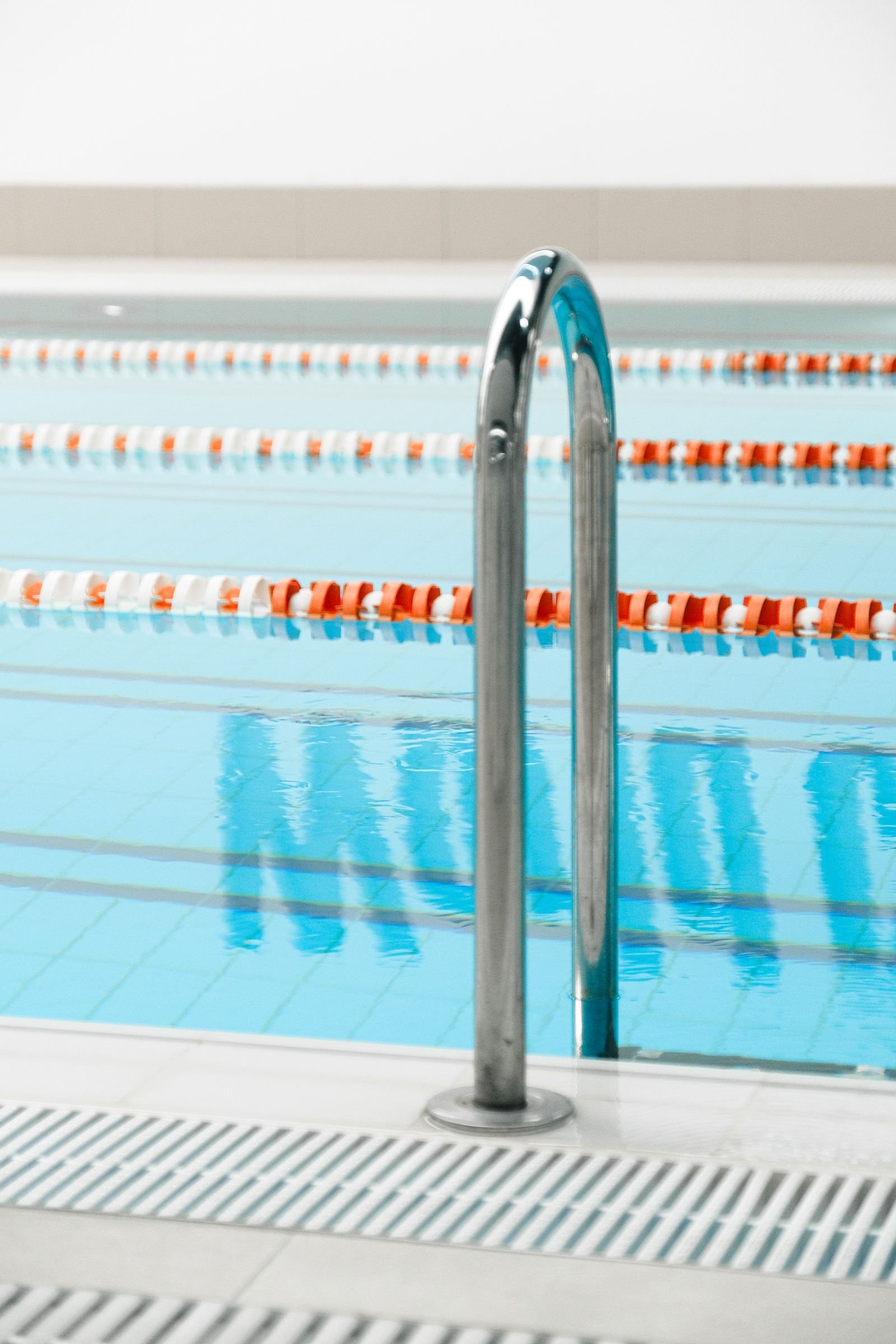 Close-up of a stainless steel pool handrail with calm clear water alongside
